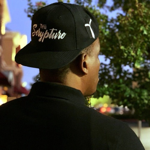 The model is wearing the black snapback cap with 3D embroidered "Trü Scrypture" on the front in a bold yet scripted font and the  picture also displays the Fashion Book logo on the side.