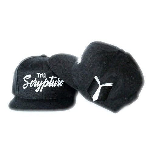 A picture of two black snapback caps with 3D embroidered "Trü Scrypture" on the front in a bold yet scripted font. The cap also features the Trü Scrypture Fashion Book logo on the left side of the cap.