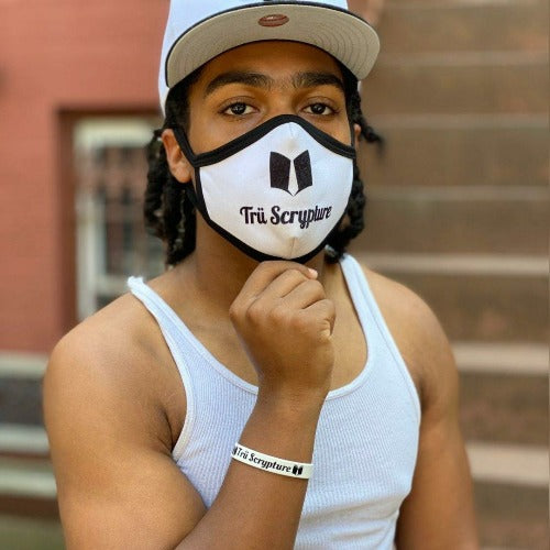 A picture of a model in the Trü Scrypture white face mask with the Trü Scrypture Fashion Book logo and name on the mask with black trim on the edges of the mask.